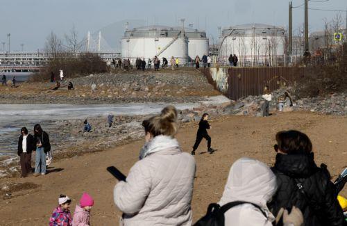 epa12841563 People walk on the shore of the Gulf of Finland with the St. Petersburg Oil Terminal in the background on a sunny day in St. Petersburg, Russia, 22 March 2026. Temperatures in St. Petersburg, Russia's second largest city, reached eleven degrees Celsius.  EPA/ANATOLY MALTSEV