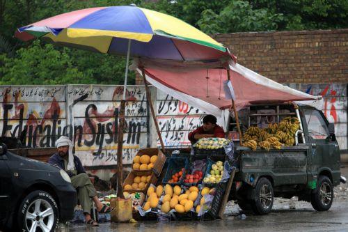 epa12860022 A vendor takes shelter under a waterproof plastic sheet during a rainy day in Peshawar, Pakistan, 30 March 2026. At least nine people were killed and several others injured after heavy rains and strong winds caused roof collapses in parts of Khyber Pakhtunkhwa and Punjab, with Bannu among the worst affected. Rescue efforts are ongoing, and...