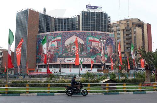 epa12861672 An Iranian man rides a motorbike past a large-scale political banner at the Valiasr square in Tehran, Iran, 31 March 2026. A joint US and Israeli military operation, launched on 28 February, continues to target strategic sites across Iran.  EPA/ABEDIN TAHERKENAREH
