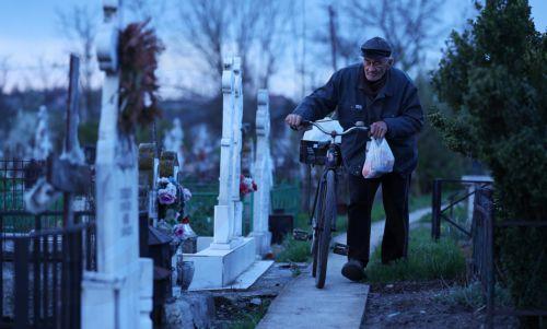 epa12876906 An elderly man pushes his bike through the graves toward his family's grave during the Orthodox Maundy Thursday memorial for the departed at a cemetery in Copaciu, Romania, 09 April 2026. Orthodox believers in the village traditionally gather in the early morning to light fires, sprinkle water and smoke over family graves, and share food in...