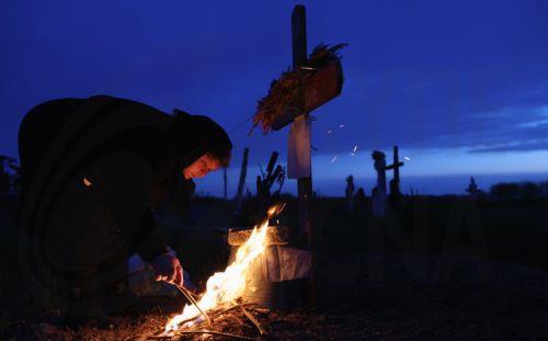 epa12876907 A woman lights a fire of dry branches during the Orthodox Maundy Thursday memorial for the departed at a cemetery in Copaciu, Romania, 09 April 2026. Orthodox believers in the village traditionally gather in the early morning to light fires, sprinkle water and smoke over family graves, and share food in memory of their departed relatives....