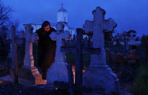 epa12876908 A woman mourns at her relative's grave after lighting a fire of dry branches during the Orthodox Maundy Thursday memorial for the departed at a cemetery in Copaciu, Romania, 09 April 2026. Orthodox believers in the village traditionally gather in the early morning to light fires, sprinkle water and smoke over family graves, and share food in...