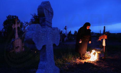epa12876909 A woman mourns at her family's grave after lighting a fire of dry branches during the Orthodox Maundy Thursday memorial for the departed at a cemetery in Copaciu, Romania, 09 April 2026. Orthodox believers in the village traditionally gather in the early morning to light fires, sprinkle water and smoke over family graves, and share food in...