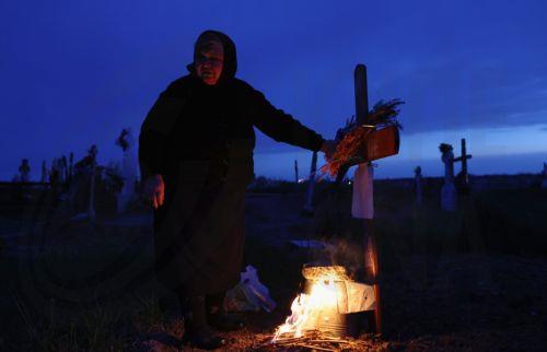 epa12876912 A woman mourns at her family's grave after lighting a fire of dry branches during the Orthodox Maundy Thursday memorial for the departed at a cemetery in Copaciu, Romania, 09 April 2026. Orthodox believers in the village traditionally gather in the early morning to light fires, sprinkle water and smoke over family graves, and share food in...