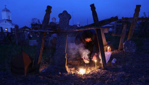 epa12876914 A woman spreads incense smoke over her family grave during the Orthodox Maundy Thursday memorial for the departed at a cemetery in Copaciu, Romania, 09 April 2026. Orthodox believers in the village traditionally gather in the early morning to light fires, sprinkle water and smoke over family graves, and share food in memory of their departed...