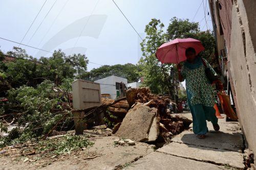 epa12923714 A woman walks past uprooted trees and broken branches following heavy overnight rain in Bangalore, India, 30 April 2026. The city was affected by over 111.5 mm of rainfall and strong winds on 29 April. More than 170 trees were uprooted, and many branches were broken due to lightning and thunderstorms. At least 10 people lost their lives in...