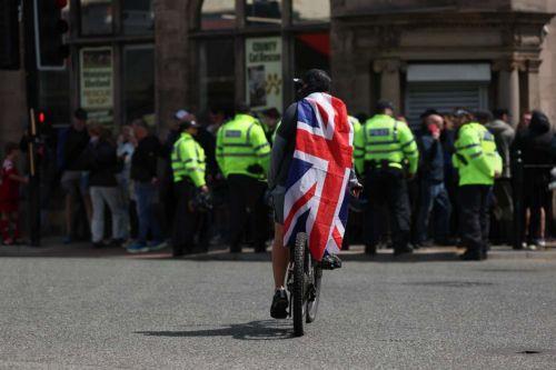 epa13034193 An anti-immigration protester cycles past police on County Road in Liverpool, Britain, 13 June 2026. Anti-immigration protesters calling for 'mass deportation' were met by counter-protesters on County Road, where a community library was burned down during rioting in the wake of the Southport murders in 2024.  EPA/STRINGER