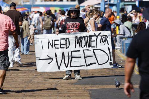 epa13125746 A person holds a sign reading 'I need money for weed' on the Santa Monica Pier in Santa Monica, California, USA, 21 July 2026. A heat wave sweeping across Southern California has brought high temperatures to the region, prompting people to seek relief at the coast.  EPA/CHRIS TORRES