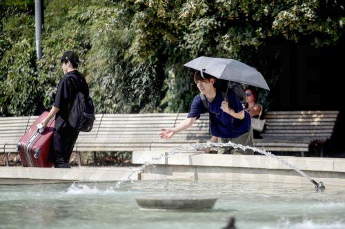 epa13143865 A person shelters from the sun under an umbrella on a hot summer day in Milan, Italy, 31 July 2026. The Italian Ministry of Health issued a 'red-dot' heatwave alert for 19 cities starting 01 August. By 02 August, the number of cities under red alert is expected to increase to 23 out of the 27 being monitored.  EPA/MOURAD BALTI TOUATI