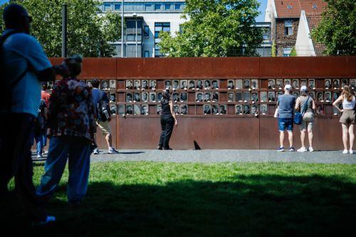 epa13166443 Visitors look at portraits of victims of the Berlin Wall that are part of an installation, decorated with flowers, at the Berlin Wall Memorial after the 65th anniversary commemoration of the construction of the Berlin Wall in Berlin, Germany, 13 August 2026. Some 65 years ago, on 13 August 1961, the Berlin Wall construction started.  EPA/CLEMENS...