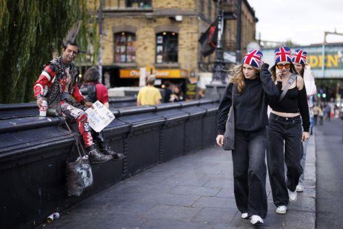 epa13188614 Tourists wearing Union Jack hats walk past a punk styled street performer as people visit Camden Town in north London, Britain, 24 August 2026. Camden Town is one of LondonÕs most culturally significant neighbourhoods, renowned for its alternative music, arts and fashion scene and its long-standing influence on British youth culture.  EPA/TOLGA...