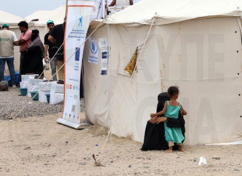 epa13246546 A displaced woman and her child (R) stand next to a shelter as UN relief groups (L) distribute aid to displaced people at a makeshift camp for Internally Displaced Persons (IDPs) in the southern port city of Aden, Yemen, 17 September 2026. At least 125,000 Yemenis have been displaced over the past two weeks amid the country’s renewed fighting...