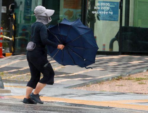epa10192694 A woman struggles to hold onto her umbrella in strong winds brought by the powerful Typhoon Nanmadol near a port in Busan, South Korea, 19 September 2022, as the powerful Typhoon Nanmadol, the 14th this season, is projected to hit the country's southeastern part later in the day.  EPA/YONHAP SOUTH KOREA OUT