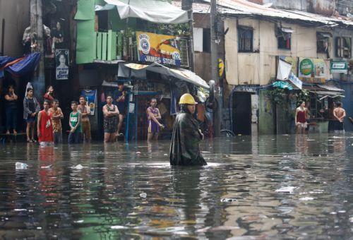 epa10830342 A man walks along a flooded road while other residents look out from their homes in Quezon City, Metro Manila, Philippines, 31 August 2023. Typhoon Saola, which has left the Philippine Area of Responsibility, and Tropical Storm Haikui off the coast of extreme northern provinces are enhancing a southwest monsoon bringing rains in the western...