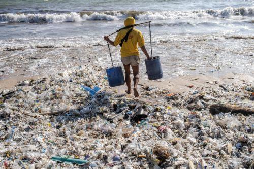 epa11229255 A man carrying buckets walks along a beach littered with piles of debris and plastic waste at the Kedonganan beach in Bali, Indonesia, 19 March 2024. Most of the trash ends up in the sea every rainy season due to the island's lack of a centralized waste management system.  EPA/MADE NAGI