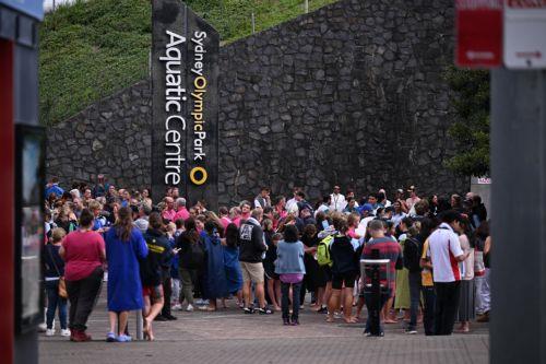 epa11336415 Evacuated patrons at the scene of a fire at Sydney Olympic Park Aquatic Centre in Sydney, Australia 13 May 2024. Fire-damaged solar panels can be seen on the roof of the swimming center which was home to the Aquatics competition during the Sydney 2000 Olympic Games.  EPA/DEAN LEWINS AUSTRALIA AND NEW ZEALAND OUT