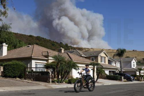 epa11597690 A person bikes down a road as the â€˜Airport Fireâ€™ continues to burn in Trabuco Canyon, California, USA, 10 September 2024. The quick-moving brush fire that ignited Monday afternoon in Orange County, before growing to more than 34,000 acres as of Tuesday night, according to Cal Fire, has triggered mandatory evacuations in both Orange and...