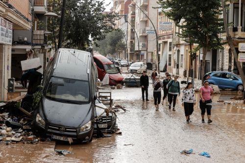 epa11692546 Residents walk past damaged vehicles piled up on a street in the flood-hit city of Valencia, eastern Spain, 30 October 2024. The intense rainfall impacting the eastern part of the country resulted in at least 70 lives being lost in the province of Valencia and neighboring provinces due to the flooding. The State Meteorological Agency (AEMET) has...