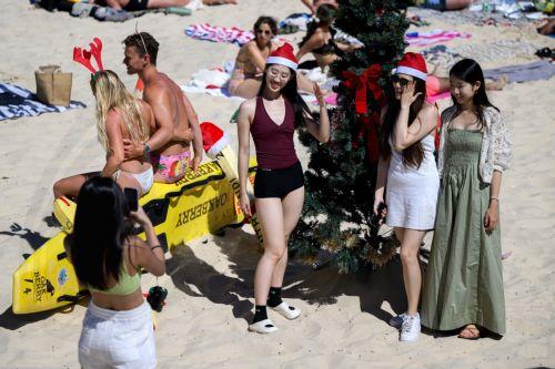 epa11792670 People wear Santa hats as they pose for a photograph with a Christmas tree at Bondi Beach in Sydney, Australia, 25 December 2024.  EPA/BIANCA DE MARCHI AUSTRALIA AND NEW ZEALAND OUT