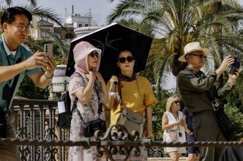 epa12144785 Several tourists protect themselves with scarves, sunglasses, and an umbrella from the sun amid an extreme heatwave as they visit the city of Seville, southern Spain, 30 May 2025. Temperatures are expected to reach 40 degrees Celsius in Seville on 30 and 31 May 2025, according to the Met Office.  EPA/JOSE MANUEL VIDAL