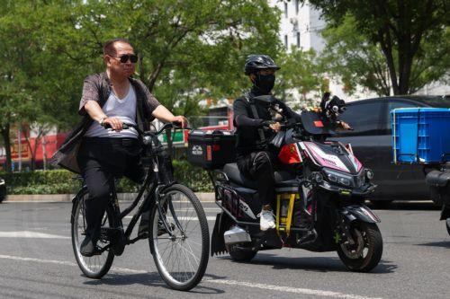 epa12192063 People ride scooters along a street during hot weather in Beijing, China, 23 June 2025. The city issued an orange alert for high temperatures as the mercury was expected to reach 38 degrees Celsius within 24 hours, according to the Beijing Meteorological Observatory.  EPA/WU HAO