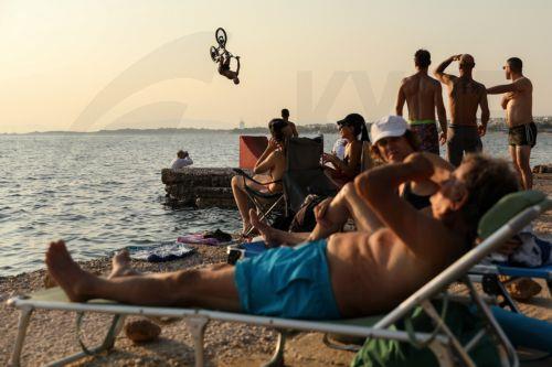 epa12248122 A BMX rider dives into the water after riding his bike over a ramp that was set up by the sea, during a heatwave at Kavouri beach, near Athens, Greece, 19 July 2025.  EPA/GEORGE VITSARAS