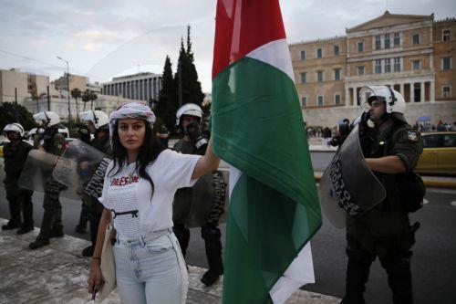 epa12275620 A Palestinian living in Greece holds a Palestinian flag in front of police officers as she takes part in a rally against Israel's ongoing operations in the Gaza Strip, in central Athens, Greece 31 July 2025.  EPA/YANNIS KOLESIDIS