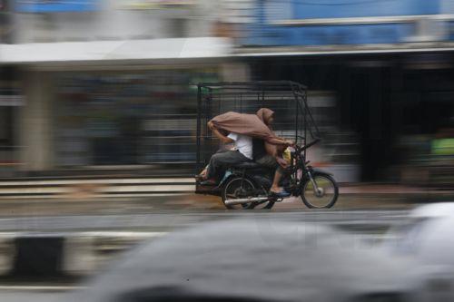 epa12549213 Motorist using a raincoat for shelter drive under heavy rain in Banda Aceh, Indonesia, 26 November 2025. The Meteorology, Climatology, and Geophysics Agency (BMKG) issued an early warning for extreme weather across the island of Sumatra, from Aceh to West Sumatra. The severe weather, including heavy rainfall with high intensity, has caused...
