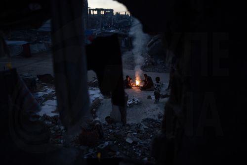 epa12618092 Displaced Palestinians warm themselves near a fire among the ruins of their destroyed home in Khan Yunis, southern Gaza Strip, 30 December 2025, amid a ceasefire between Israel and Hamas.  EPA/HAITHAM IMAD