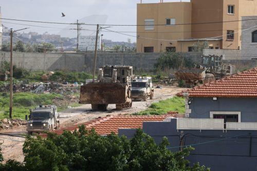 epa12644860 Israeli army bulldozers pass buildings during a military operation in Nur Shams refugee camp, near the West Bank city of Tulkarem, 12 January 2026. Israeli troops continue their operation in the Nur Shams refugee camp, east of Tulkarem, which has been under a tight Israeli siege since January 2025.  EPA/ALAA BADARNEH