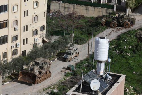 epa12644867 Israeli army bulldozers pass buildings during a military operation in Nur Shams refugee camp, near the West Bank city of Tulkarem, 12 January 2026. Israeli troops continue their operation in the Nur Shams refugee camp, east of Tulkarem, which has been under a tight Israeli siege since January 2025.  EPA/ALAA BADARNEH