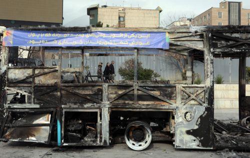 epa12650627 Iranians walk near the wreckage of a burnt-out public bus in Tehran, Iran, 15 January 2026. The country remains under a near-total nationwide internet blackout that began on 08 January, amid an intensifying wave of anti-government protests.  EPA/ABEDIN TAHERKENAREH