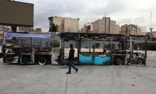 epa12650629 An Iranian man walks near the wreckage of a burnt-out public bus in Tehran, Iran, 15 January 2026. The country remains under a near-total nationwide internet blackout that began on 08 January, amid an intensifying wave of anti-government protests.  EPA/ABEDIN TAHERKENAREH