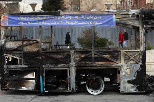 epaselect epa12650601 Iranians walk near the wreckage of a burnt-out public bus in Tehran, Iran, 15 January 2026. The country remains under a near-total nationwide internet blackout that began on 08 January, amid an intensifying wave of anti-government protests.  EPA/ABEDIN TAHERKENAREH