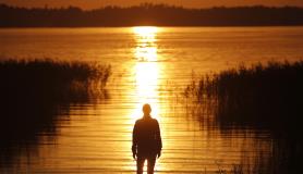 Άντρας παρακολουθεί το ηλιοβασίλεμα πάνω από τη λίμνη στο Aluksne, Λετονία